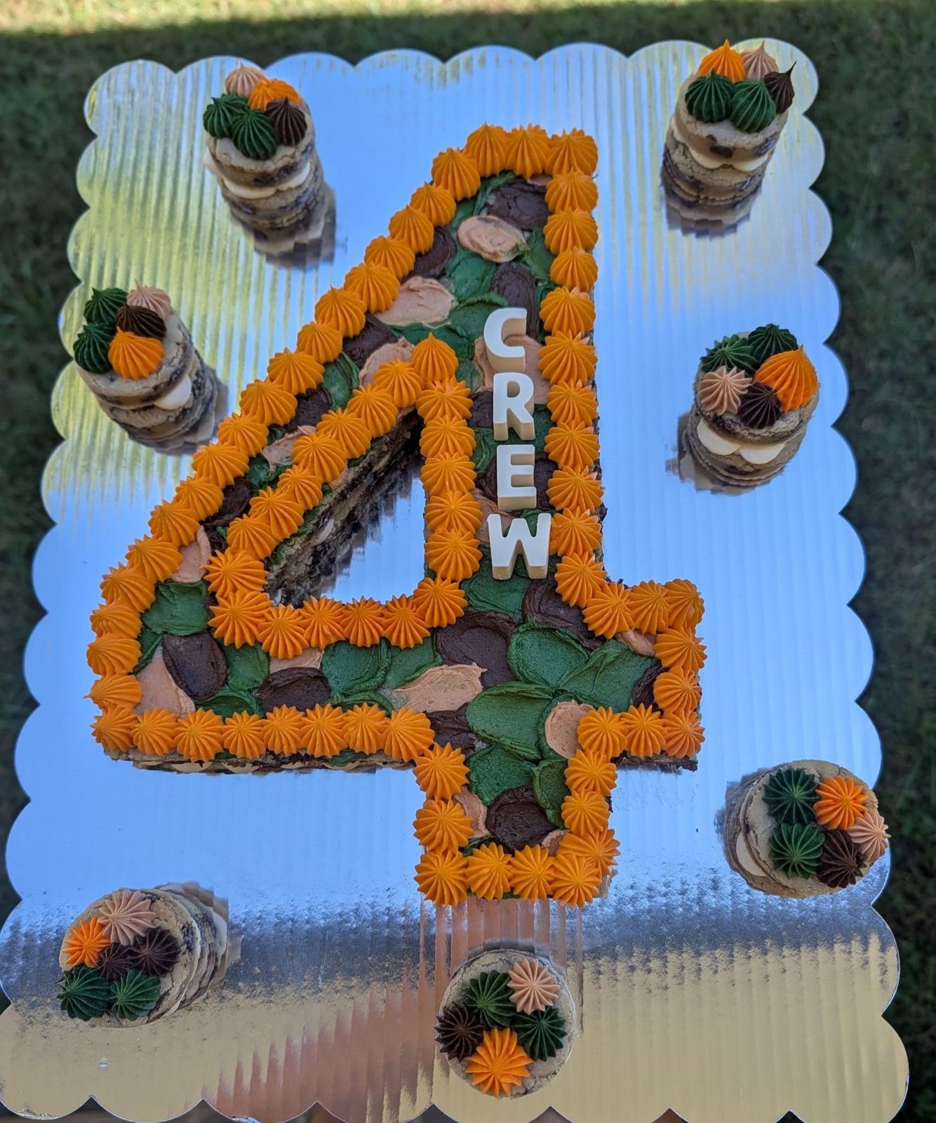 Camo-themed double-layer number 4 cookie cake with orange stars and the name CREW